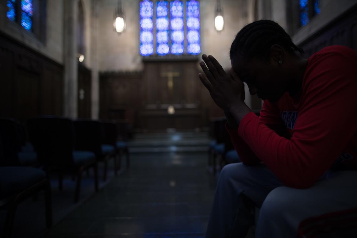 Male student bowing his head in prayer in Danforth Chapel