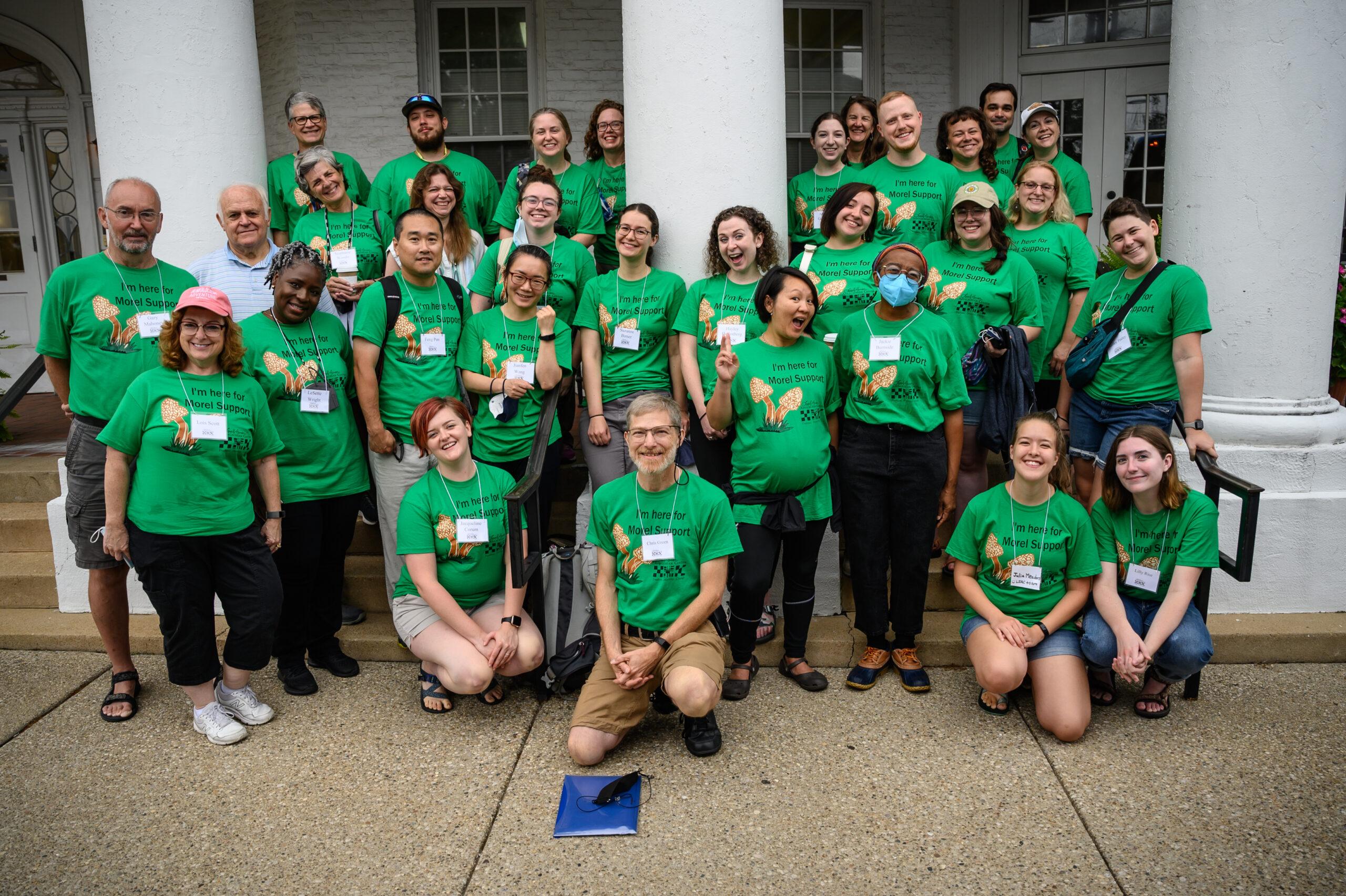 A group of faculty and staff of Berea College, posing for a group picture in front of Boone Tavern, as they are preparing to embark on the Appalachian Tour, organized by the Loyal Jones Appalachian Center. All participants are wearing matching green shirts.